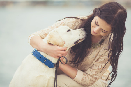 portrait of beautiful young woman playing with dog on the sea shore